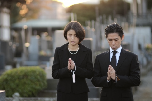 墓前に手を合わせる夫婦